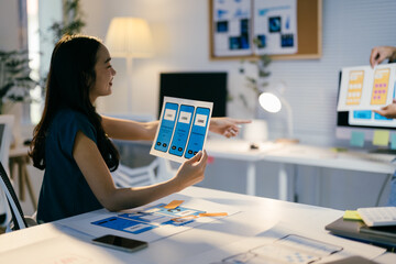 Ui designer is holding a prototype of a mobile application and showing it to her colleague during a...