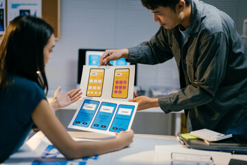 Two designers deeply engrossed in conversation about mobile app templates, analyzing user experience and interface elements in a modern office space