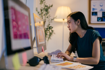 Young woman designer works late at night in her home office, focused on meeting a deadline for her...