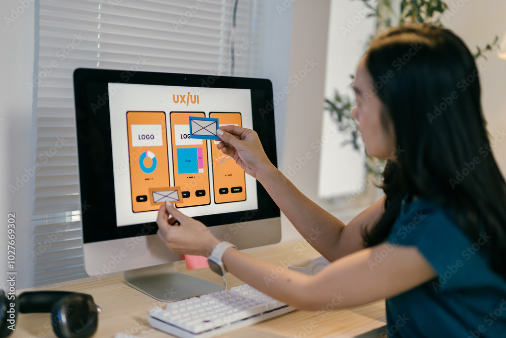Poster Young web designer is working on a user interface, arranging different elements of a mobile app on her computer screen