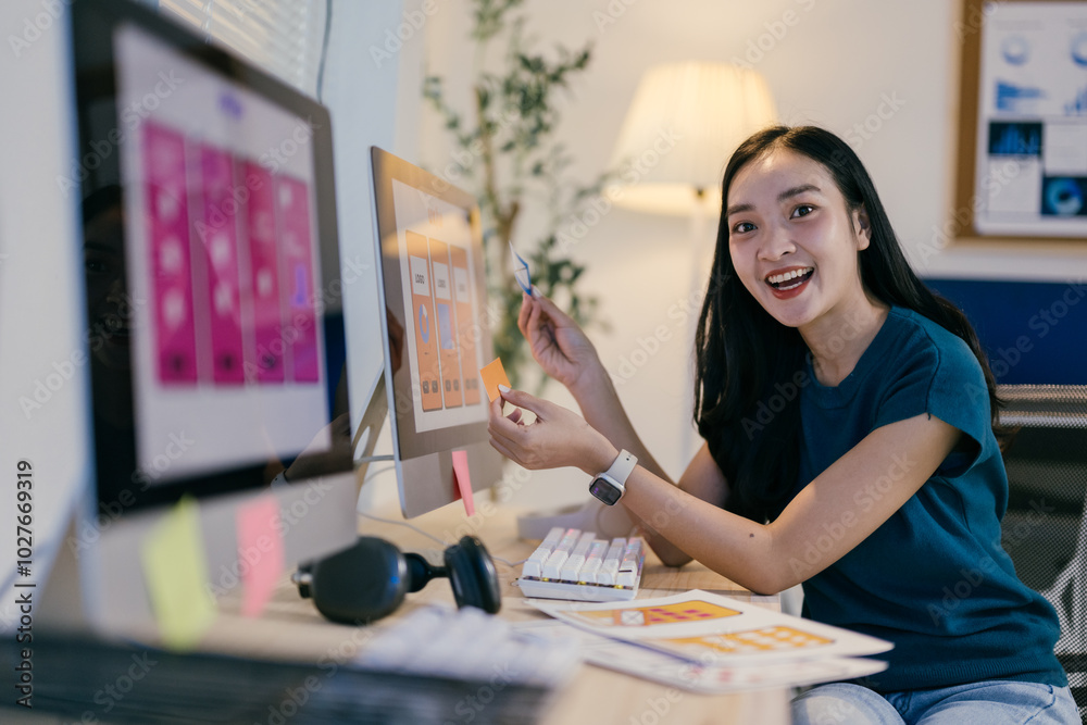 Poster Ui designer is using sticky notes while working on a mobile application in her office. She is smiling and looking happy with her work