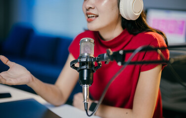 Young woman is recording a podcast in her home studio, speaking into a professional microphone and...