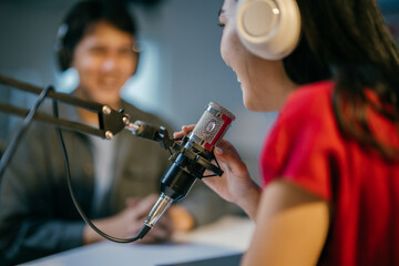 Young woman is hosting a radio show, speaking passionately into a professional microphone while her guest listens attentively in the background