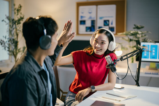 Two young content creators are giving high five while recording audio podcast at home studio together. They are happy and enjoying in their job