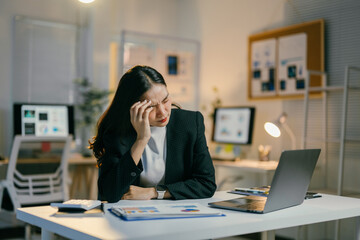 Stressed businesswoman working late in dimly lit office, feeling exhausted and pressured, focused on meeting deadline despite burnout