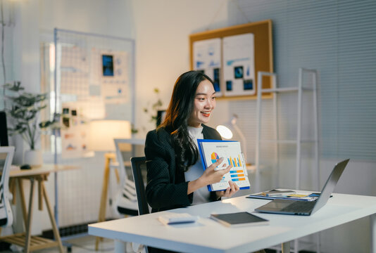 Businesswoman is presenting charts and data analysis while having a video conference with her team on a laptop in the office at night