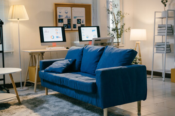 Modern office space is illuminated by natural light and lamps, featuring a blue couch and multiple computer monitors displaying graphs