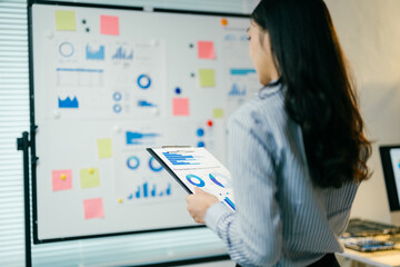 Businesswoman is holding a clipboard and analyzing financial business chart data on a report. She is standing in an office meeting room