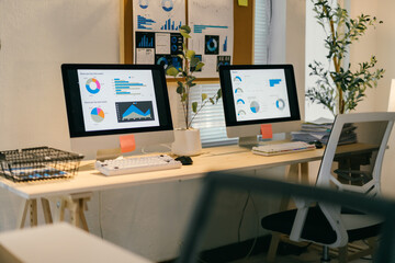 Two desktop computers are displaying financial data and charts on a desk in a modern office, suggesting a focus on data analysis and financial performance