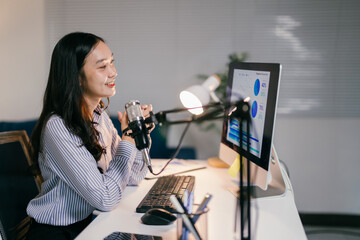 Young businesswoman recording a podcast using a professional microphone, sitting at her desk and...
