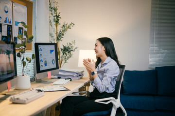 Young asia businesswoman working from home office, clapping celebrating success after looking at financial charts data on computer screen