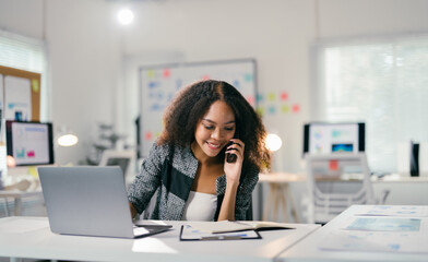 Young manager is working in a luminous open space and handling business on the phone, she is smiling and seems focused