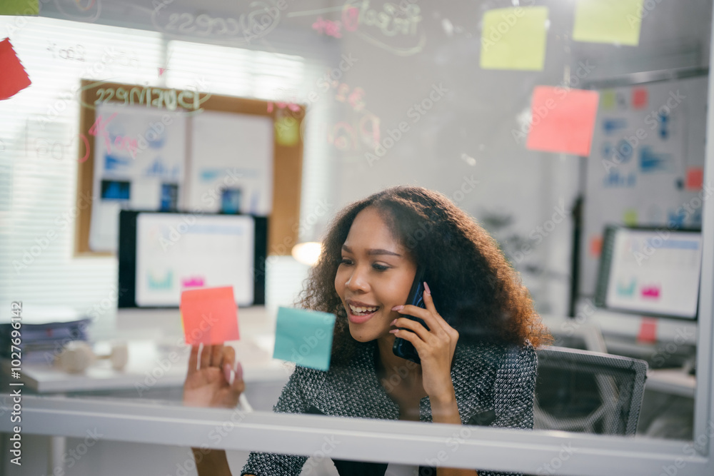 Poster young businesswoman is smiling while talking on the phone and using adhesive notes to plan a project