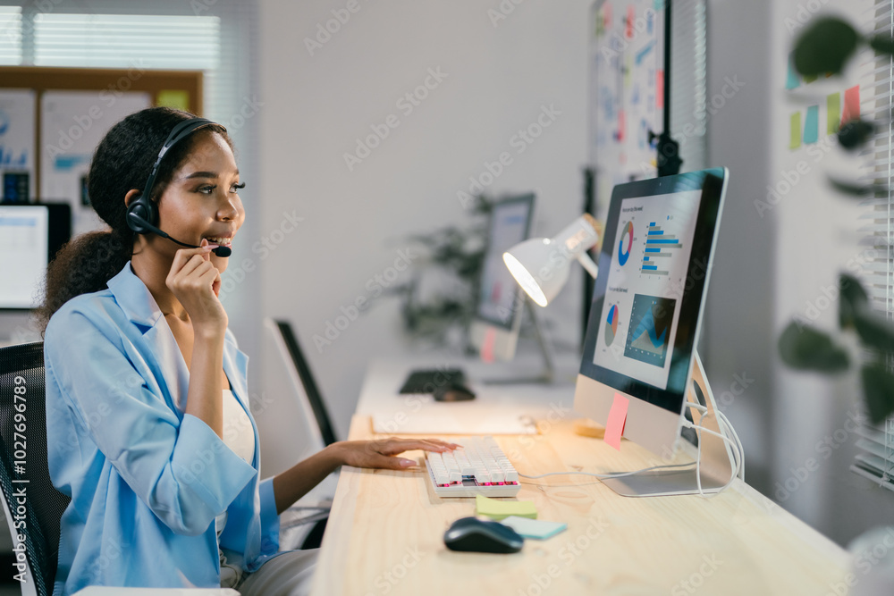 Poster young professional woman is speaking into a headset while working late at the office. she is typing 