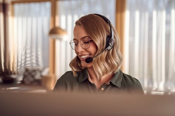 Young Bavarian woman with blonde wavy hair, wearing glasses and a headset, smiling while working in a bright home office, casual green shirt, warm indoor setting
