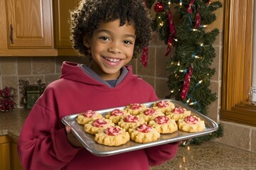 Joyful young African American boy holding a tray of holiday cookies in the kitchen.