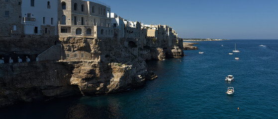 Fototapeta premium Fishing boat in the sea. Coastline. Rocky shore with buildings in Polignano a Mare, Italy.