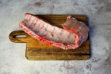 Wooden dark brown board with big piece of raw pork ribs on grey marble table in kitchen. side view. cooking. copy space