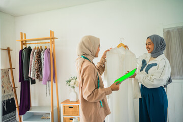 woman Muslim fashion designer in hijab shows clothes to a customer in a workshop