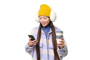 Young Asian woman wearing winter muffs over isolated chroma key background holding coffee to take away and a mobile