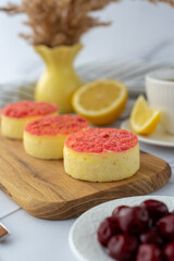 Mini cheesecakes with pink crumble topping served on a wooden board with lemons and cherries. Concept of summer dessert, fresh flavors, and artisanal pastries.