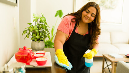 Maid with yellow gloves and a black apron cleans a wooden surface using a blue rag and cleaning...