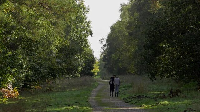 Two young mushroom pickers carying a wicker basket and wearing rubber boots are walking away from the camera