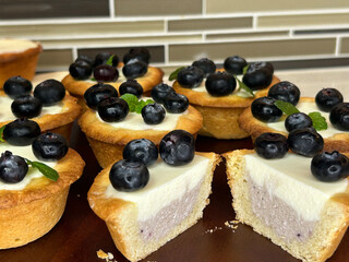 Two blueberry tartlets sliced in half reveal their creamy, smooth filling and golden-brown crust. Topped with fresh blueberries and mint, these tartlets have a perfectly baked.
