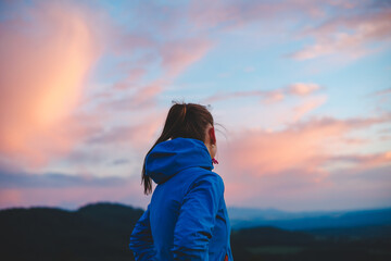 woman in a blue jacket stands against a breathtaking backdrop of pink and blue clouds at sunset....