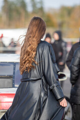 A woman with long brown hair is walking down the street wearing a black coat