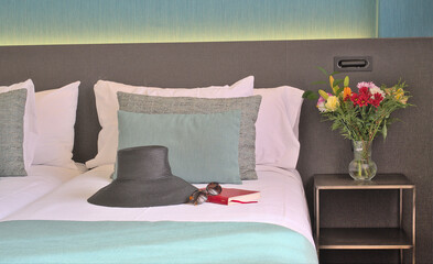  Hat, sunglasses, and book placed on bed with fresh flowers in a modern hotel room