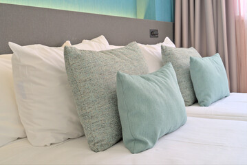  Three decorative pillows are neatly placed on a hotel bed, with soft turquoise colors and a modern backdrop of gray and teal tones.