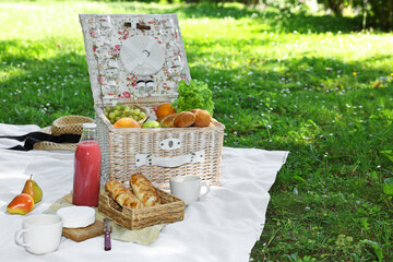 Picnic wicker baskets with delicious food, tableware and drink on white blanket outdoors