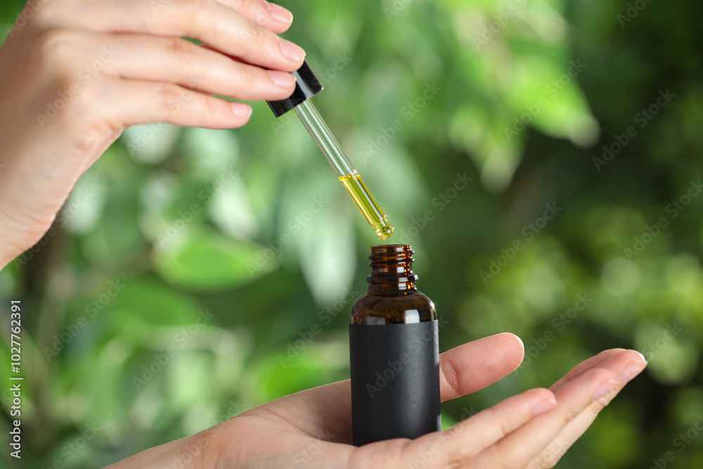 Canvas Prints Woman dripping tincture from pipette into bottle against blurred green background, closeup