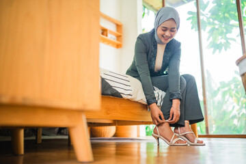 Muslim woman office worker in hijab wearing shoes getting ready before work in a room