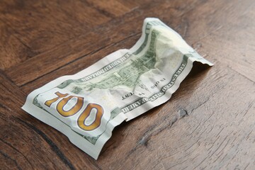 One crumpled dollar banknote on wooden table, closeup
