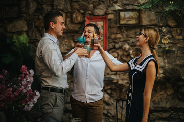 Three happy friends cheerfully toasting with vibrant cocktails in an outdoor setting, enjoying friendship and celebration in a lively atmosphere.