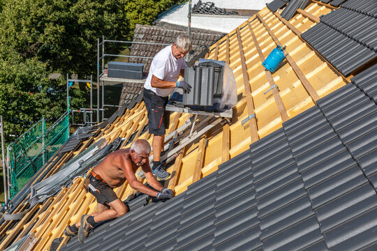 Ein Dach wird neu gedeckt. Beton-Dachsteine in der Farbe Anthrazit. Zwei Dachdecker im Seniorenalter