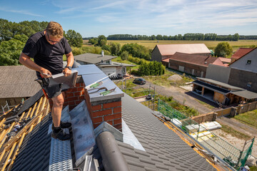 Ein Dach wird neu gedeckt. Anthrazitfarbene Beton-Dachsteine. Die alten Schornsteine bekommen eine Abdeckung aus Edelstahl