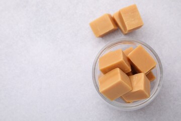 Tasty sweet caramel candies in glass jar on light table, top view. Space for text