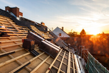 Ein Dach wird neu gedeckt. Unterkonstruktion mit Holz-Weichfaserplatten. Anthrazitfarbene Beton-Dachsteine. Sonnenuntergang