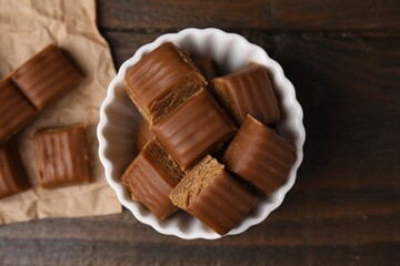 Tasty sweet caramel candies in bowl on wooden table, top view