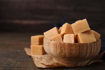 Tasty sweet caramel candies in bowl on wooden table, space for text