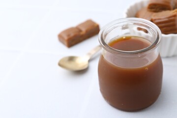 Tasty caramel sauce in jar on white table, closeup. Space for text