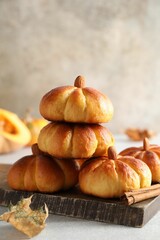 Tasty pumpkin shaped buns and cinnamon on light grey table, closeup