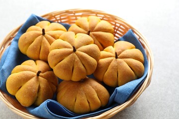 Wicker basket with tasty pumpkin shaped buns on light table, closeup