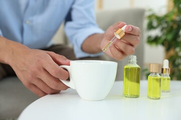 Young man dripping CBD tincture into drink at white table, closeup