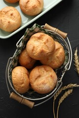Homemade tasty buns and spikelets on black textured table, flat lay