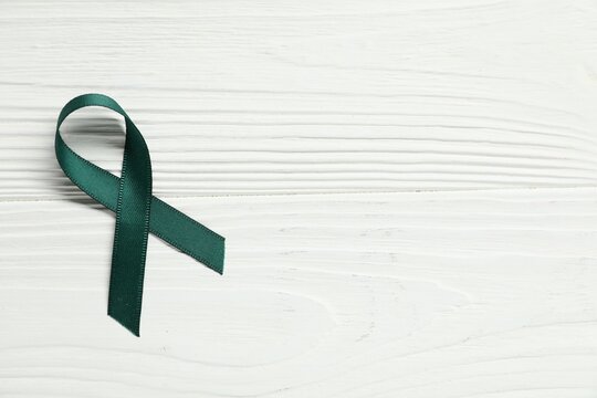 Green awareness ribbon on wooden background, top view. Space for text