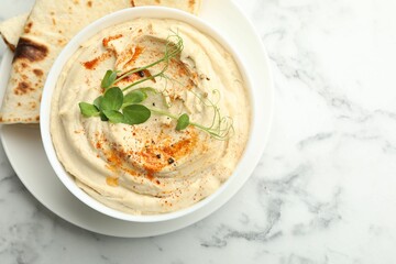 Delicious hummus with paprika and pita on white marble table, top view